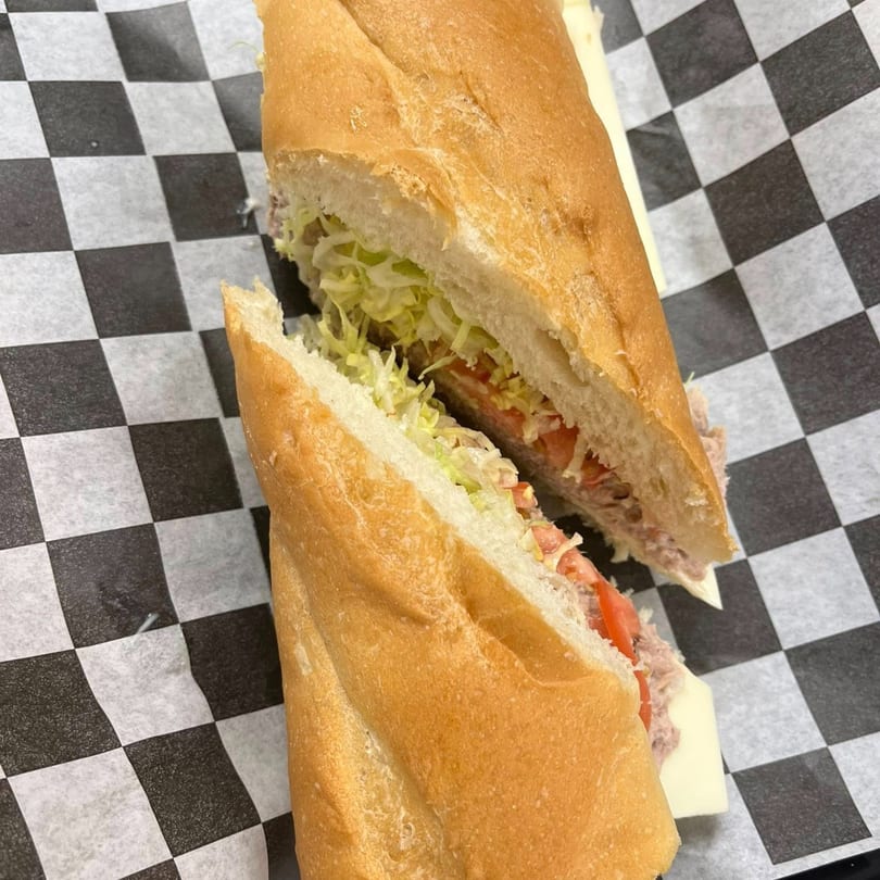 A Romeo's Italian Submarine, cut in half, revealing tuna, lettuce, tomatoes, and cheese on checkered paper.