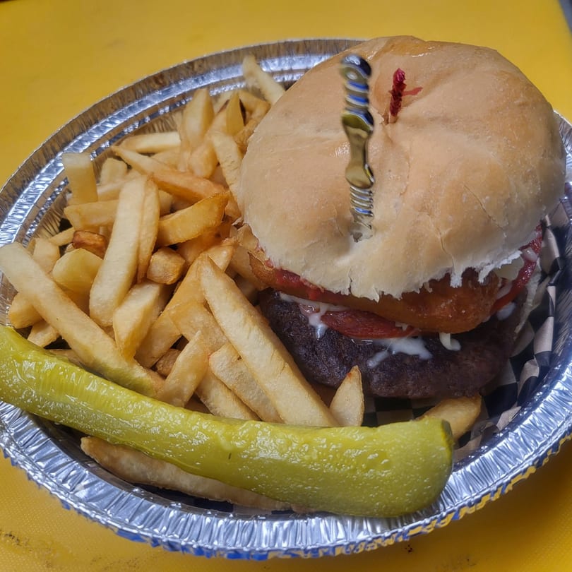 A Romeo's Italian Submarines burger with fries and a pickle spear in a foil container.